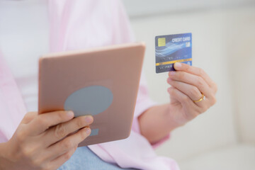 Hands of young asian woman sitting on sofa using digital tablet shopping online with credit card on couch, female paying with transaction financial, purchase and payment, business concept.