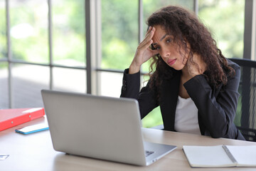 Mid adult businesswoman touching her head on table in office after bad news business failure or get fired and feeling discouraged, distraught and hopeless in modern office.