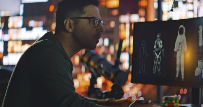 Male Engineer Developer of Space Suits and Space Gear Work in His Home Studio. Caucasian Latino Man Creating 3D Virtual Models of Spacesuits and Makes Corrections. Night City Background