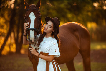 portrait of a young beautiful woman with curly hair who is holding a brown horse. Walking with the animals on the farm. Horse riding. boho style rider