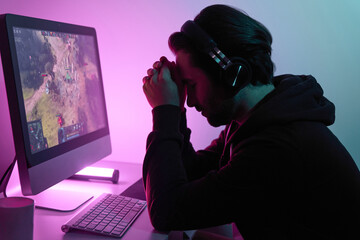 Frustrated young man leaning head on hands while playing game against colorful background