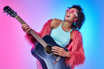 Fototapeta premium Beautiful African woman in fluffy jacket playing guitar and smiling against colorful background