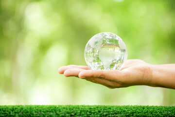 Human hand holding globe planet glass In green forest with bokeh nature lights. world environment day. concept for environment conservation, protect ecology earth and environmental eco-friendly life.