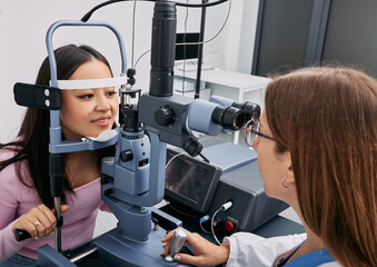 Korean woman while eye exam with binocular slit-lamp at ophthalmology clinic with experienced...
