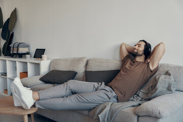 Obraz premium Handsome young man in headphones holding hands behind head while relaxing on the couch at home