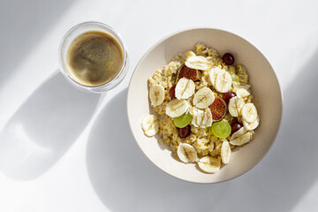 Top view of morning meal on white background. Oatmeal with fruit and cup of coffee