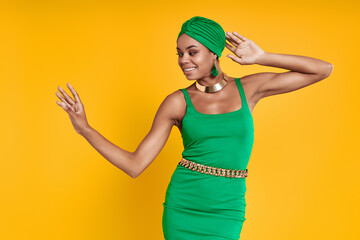 Beautiful African woman in traditional headwear dancing against yellow background