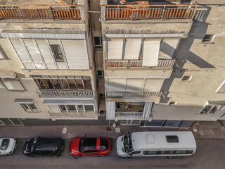 Top view of a narrow city street with parked cars in Antalya, Turkey. Facade of a multi-storey residential building with shutters on the windows and balconies, close-up