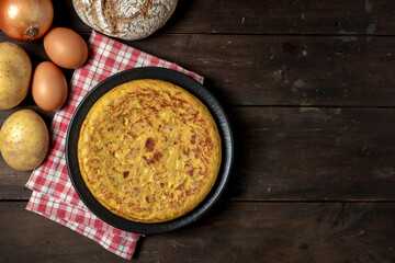 POTATOES OMELETTE AND THE INGREDIENTS ON DARK WOODEN TABLE. TYPICAL SPANISH FOOD. COPY SPACE. TOP VIEW.