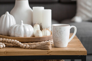 Fototapeta na wymiar Still-life. Dried pampas grass in a vase, white ceramic pumpkins, a teapot, a cup and pumpkin-shaped candles on a coffee table in the home interior of the living room. Cozy autumn concept.