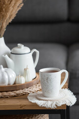 Still-life. Dried pampas grass in a vase, white ceramic pumpkins, a teapot, a cup and pumpkin-shaped candles on a coffee table in the home interior of the living room. Cozy autumn concept.