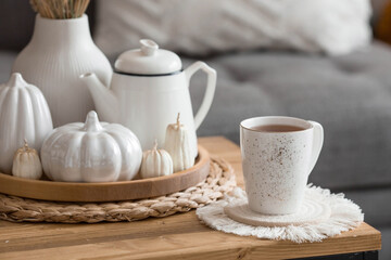Still-life. Dried pampas grass in a vase, white ceramic pumpkins, a teapot, a cup and pumpkin-shaped candles on a coffee table in the home interior of the living room. Cozy autumn concept.