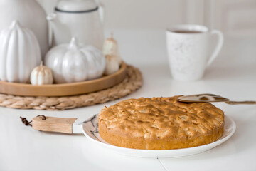 Still-life. Dried pampas grass in a vase, white ceramic pumpkins, candles and apple pie charlotte on a white table in the interior of a Scandinavian-style home kitchen. Cozy autumn concept.