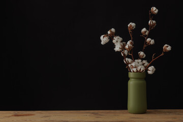 cotton flowers in a green vase on a wooden table against a dark background, mock-up