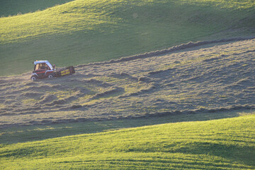 Mountain farmer rakes on the green steep slope in the evening light, slope tractor in harvest use  © Niko Troebst