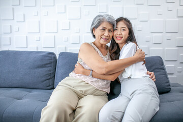 Asian grandma and granddaughter hugged with happy mood on the sofa in home.