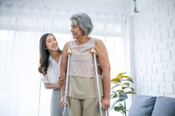 Help and care for a senior Asian grandmother or old woman using a healthy walker while walking at home.