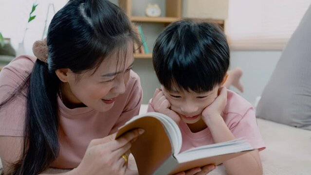 4K, Asian mother and boy, wearing a pink t-shirt, The two of them lay comfortably on the bed, A mother teaches a boy to read a book, ready to read it to his son, without serious and fun.