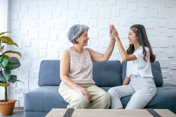 Asian grandmother and granddaughter talking and hi-five at home. Senior and young woman smiling and happy mood on sofa in living room. - 531462134