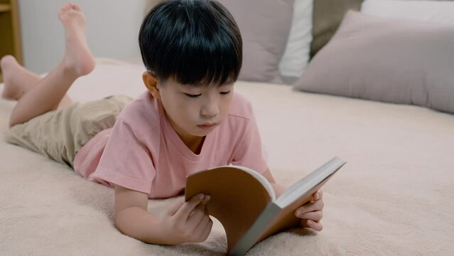 4K, An Asian boy, handsome, laying in his favorite soft bed reading a book, He quickly opened the picture in the book that was in his hand, and there was a serious expression on each page.