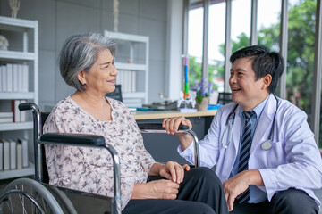 Fototapeta premium Asian doctor supporting and cheering up senior patient in wheelchair talking, smiling in comfort at home. Healthcare and medicine concept.
