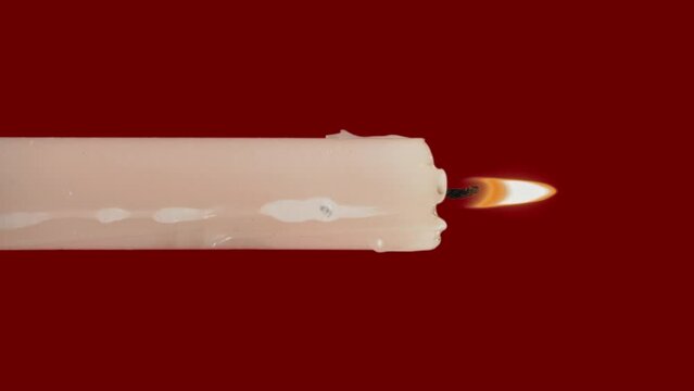 White paraffin candle with yellow tints burns on a red background. One wax candle burns motionless and emits fire.