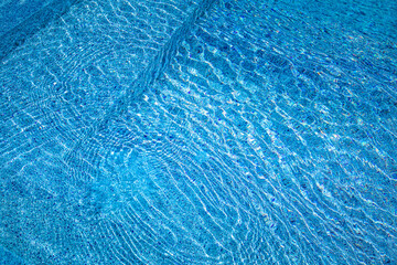 Blue shadows of pool with steps into, sunny summer mood. Ripples water surface, fun recreational outdoor sport background. Abstract swimming aqua texture, natural pattern