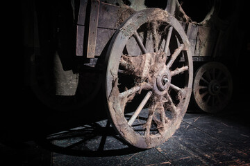 Fototapeta na wymiar A wheel of the vintage wooden wagon on the dark background