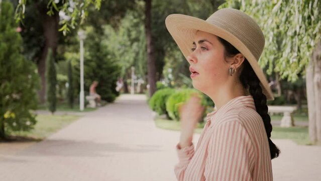 Sunstroke and heatstroke. A sweaty woman in a straw hat is standing on the street, fanning herself with her hand from the heat. Summer vacation and hot temperature.