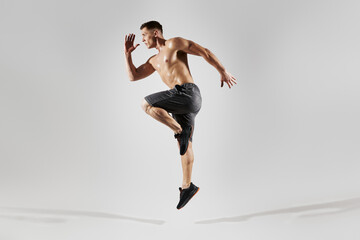Confident muscular man with perfect body jumping against white background