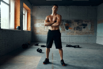 Naklejka premium Full length of handsome muscular man keeping arms crossed while standing in gym