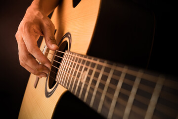 Close up hand playing acoustic guitar on black background