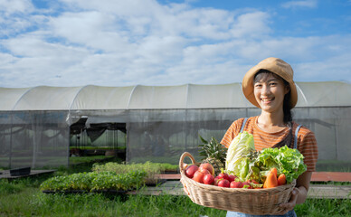 Young Asian beautiful Farmer woman holding wooden basket full of fresh raw vegetables. Basket with...