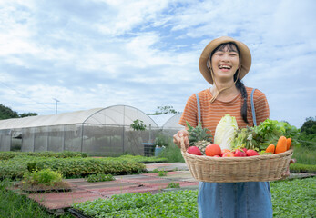 Young Asian beautiful Farmer woman holding wooden basket full of fresh raw vegetables. Basket with...