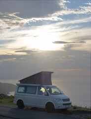Fototapeta premium Camper standing on mountain at sunset in front of the ocean