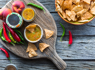 Peach and pepper salsa with tortilla chips on a rustic board and table.
