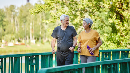 Middle-aged wife and husband wear activewear strolling along bridge
