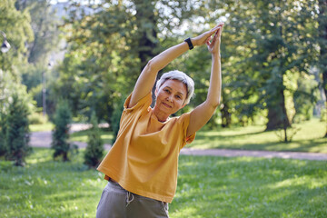 Older Asian woman makes stretching exercises in summer park
