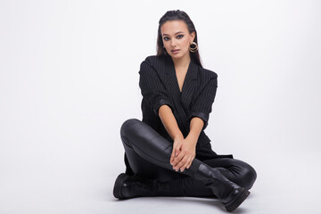 Fototapeta na wymiar Fashion photo of a beautiful elegant young woman in a pretty black jacket, leather pants, boots, posing over white background. The hair is gathered back, dark brunette. Studio Shot