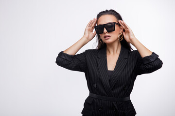 Fashion photo of a beautiful elegant young woman in a pretty black jacket, leather pants, boots, sunglasses posing over white background. The hair is gathered back, dark brunette. Studio Shot