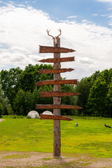 Wooden Direction Sign. Skull of a horned deer on a wooden post. Direction with inscriptions in Russian: Wild ducks; Deers; Stable-yard; Bear - Saigara; Peacock; Bear - Mishka; Camel - Fatima.