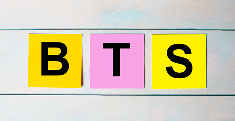 Three multi-colored paper stickers with BTS text on a blue wooden background.