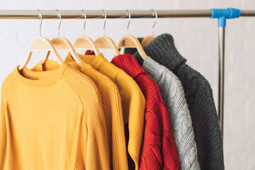 Multi-colored knitted sweaters on wooden hangers hang on an iron rack rale.