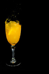 orange drink splash in glass cup on black background