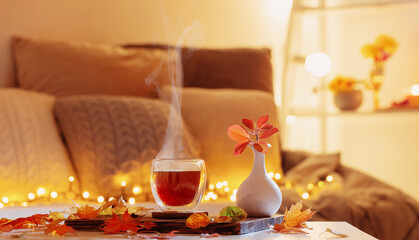 thermo glass with hot tea in dark night room with autumnal leaves