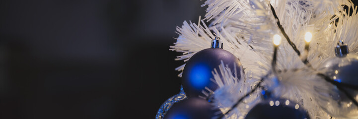 Wide view image of shiny blue holiday baubles hanging on white christmas tree