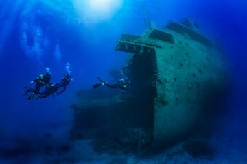 A scuba diving instructor leads a group of unrecognizable divers through a big shipwreck in the...