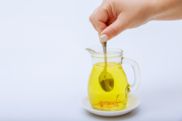 A woman stirs stamens in saffron tea in a transparent jug on a white background. Saffron tea.