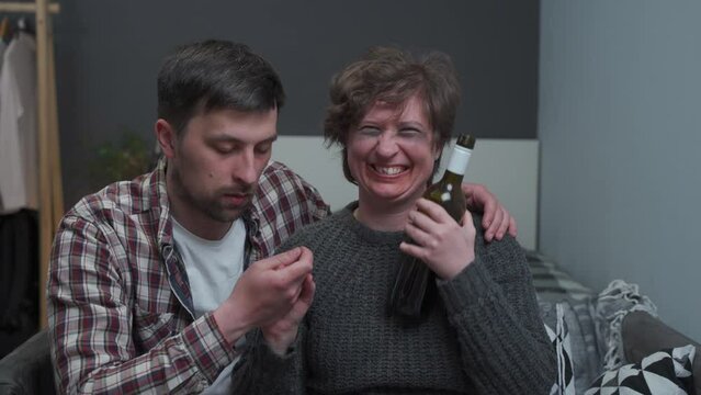 Loving husband calming his drunken crazy wife addicted to alcohol at home. Man calms down woman addicted to alcohol with bottle of wine. Male taking away wine glass from alcohol-addicted female.