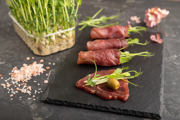 Slices of smoked salted meat with green pea microgreen on black. Side view, selective focus.